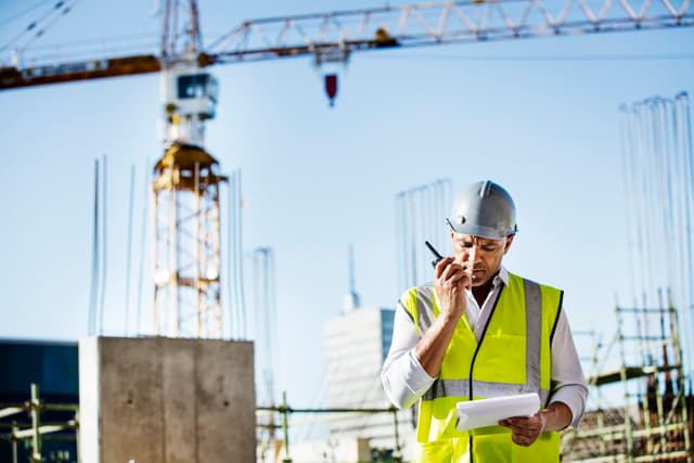 Construction worker on a walkie talkie with a crane in the background 1200x800